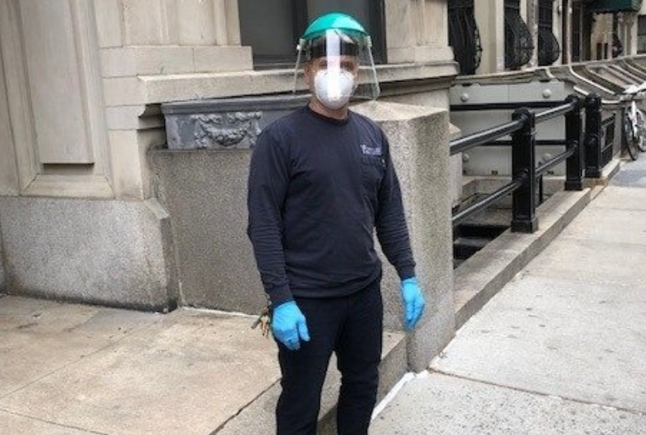 man wear face mask and plastic shield with Columbia branded long sleeve shirt in front of residential building