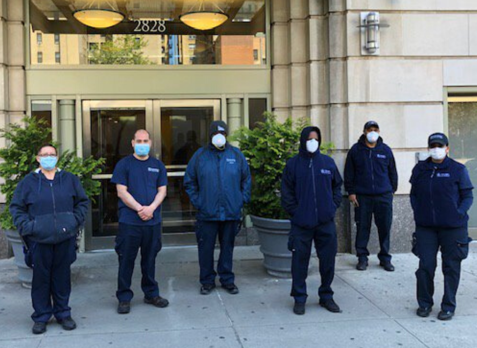 six residential staff members wearing face masks and Columbia branded jackets in front of residential building