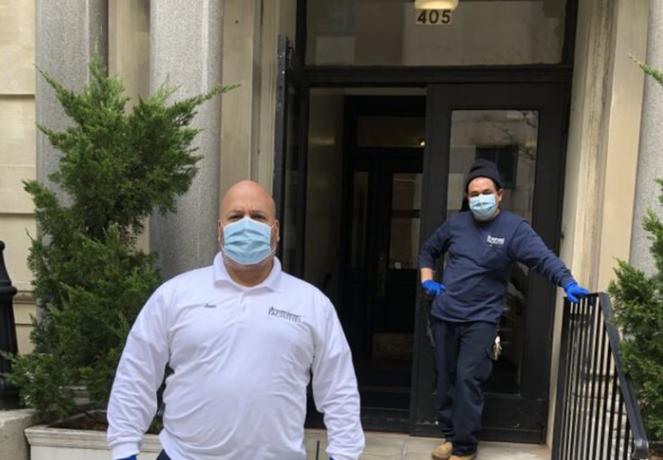two men wearing face masks in front of residential building, one with a white Columbia branded long sleeve shirt and the other with a blue Columbia branded long sleeve