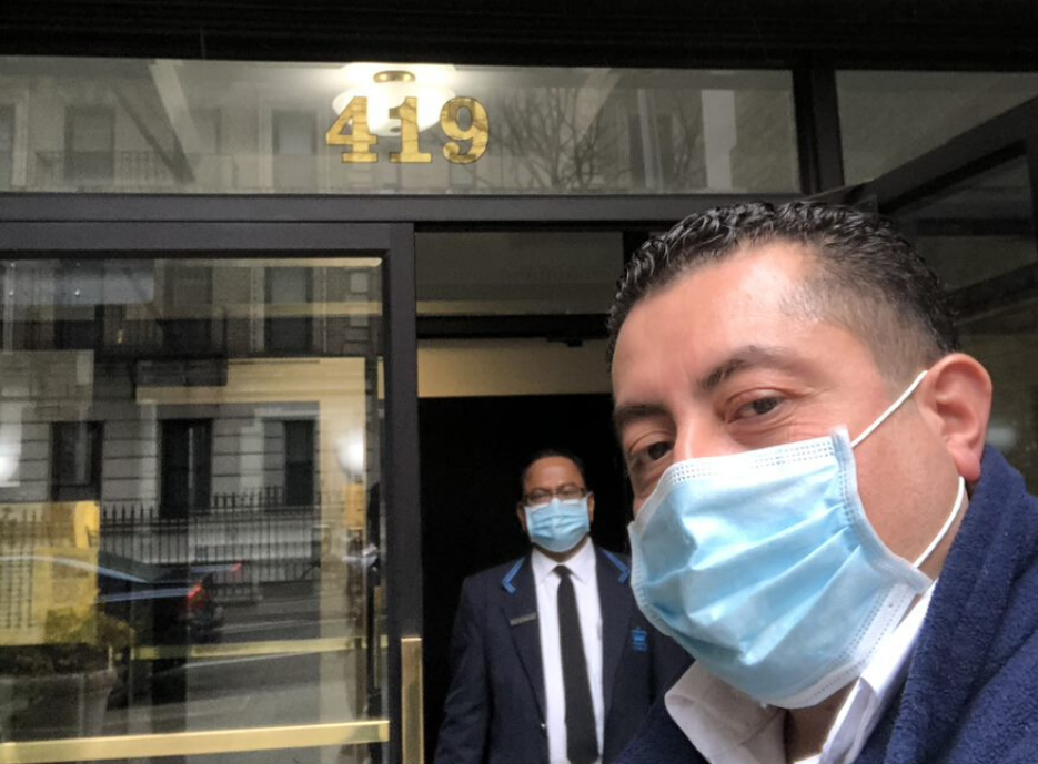 two men wearing face masks taking a selfie in front of residential building with number 419