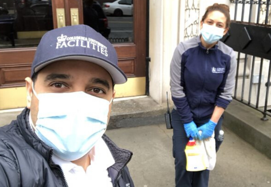 man wearing face mask and Columbia branded cap and woman wearing face mask take selfie in front of residential building