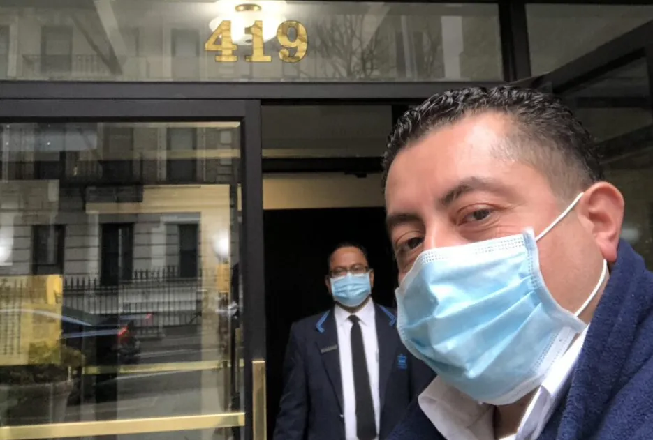 two men wearing face masks taking a selfie in front of residential building with number 419