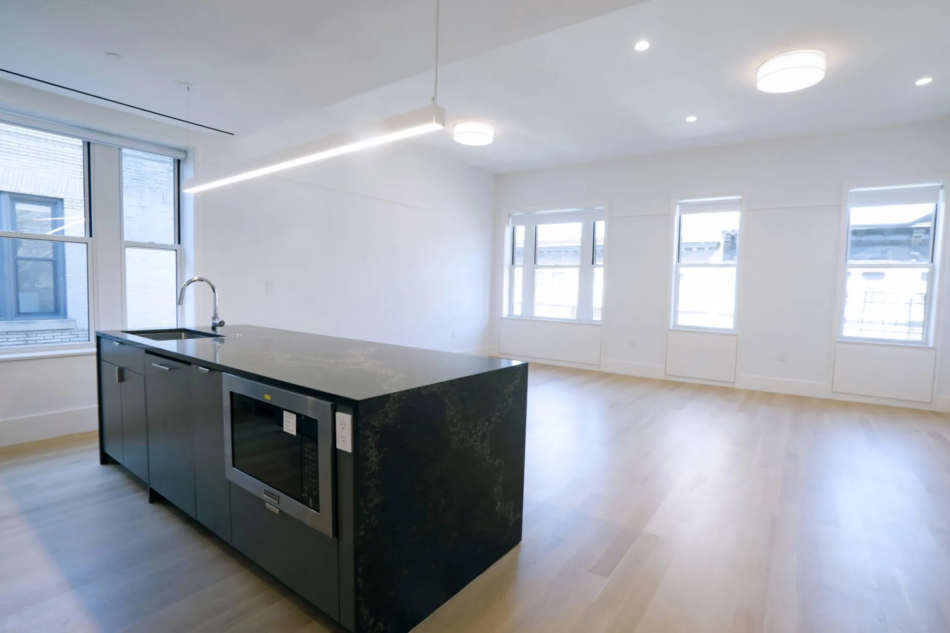 A view of the living room of a renovated apartment with a black and gold marble kitchen island.